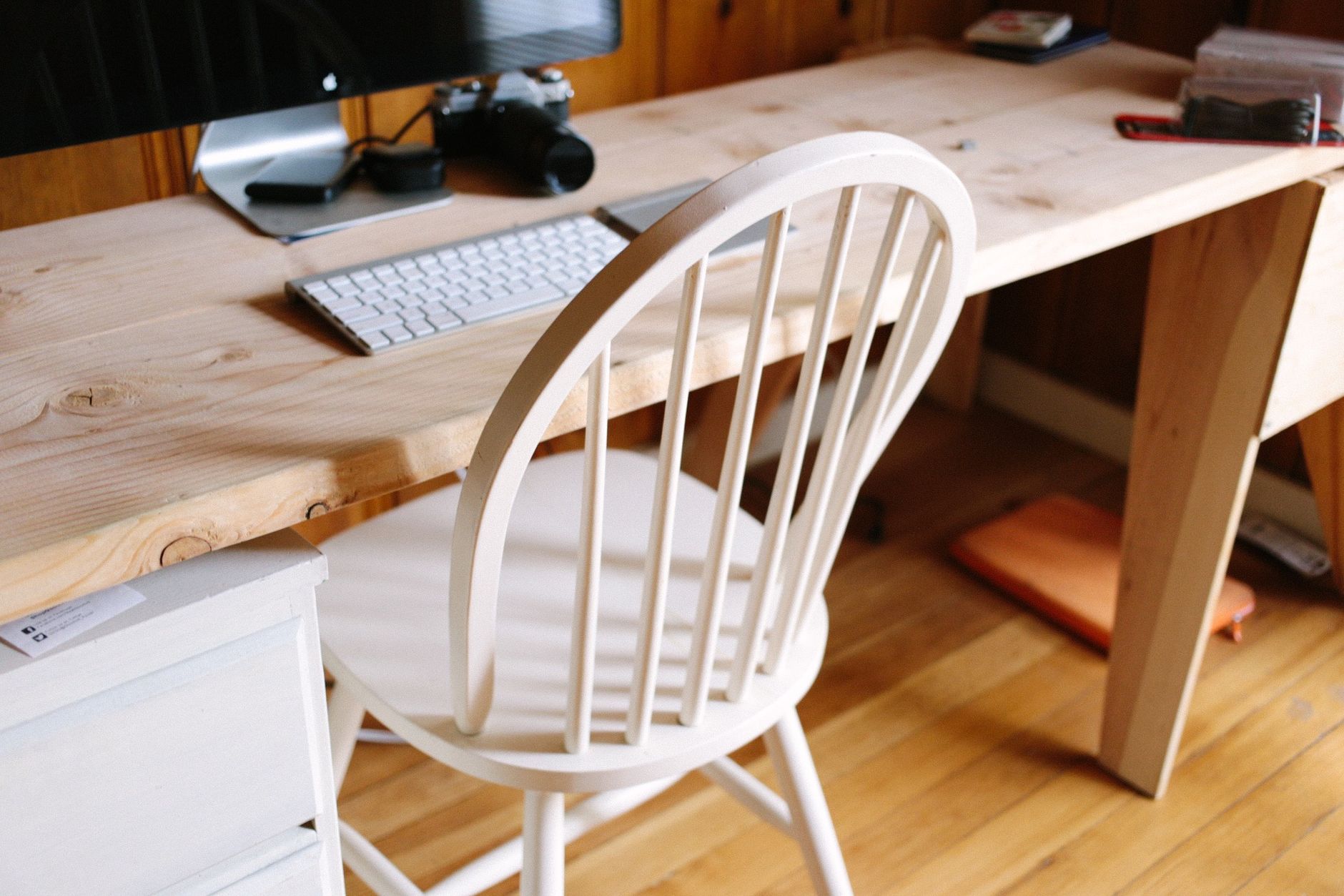 Un minimalista escritorio de oficina en casa con silla de madera, teclado y cámara.