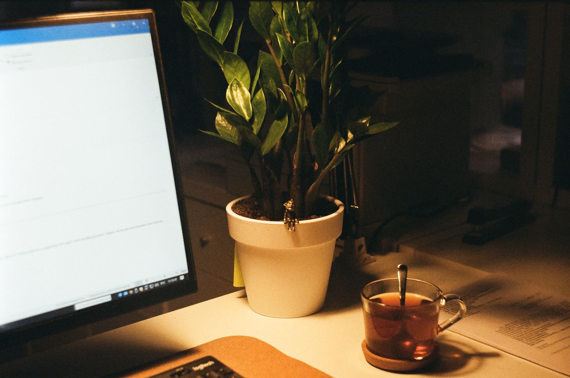 Espacio de trabajo cálido y acogedor con pantalla de ordenador, planta y una taza de té.